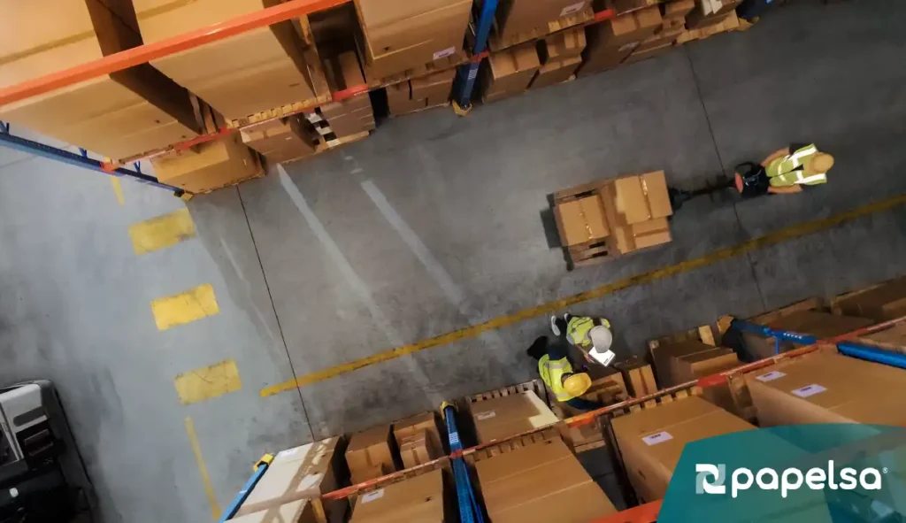 Equipo logístico gestionando productos con apoyo de lista de empaque, organizando mercancía en almacén para exportación.