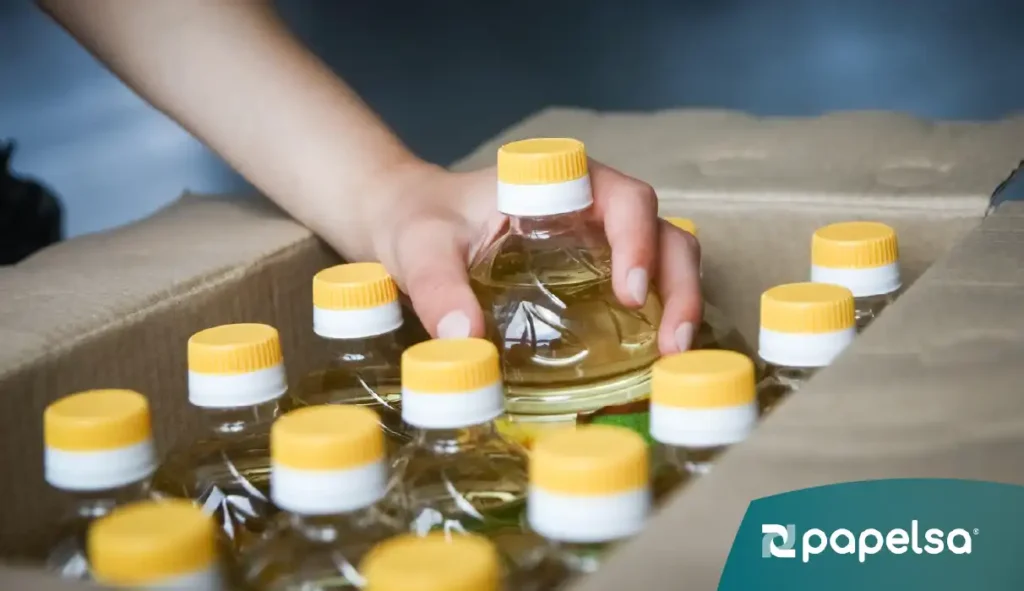 Persona tomando un producto botella de aceite con tapa amarilla en su empaque de cartón secundario.