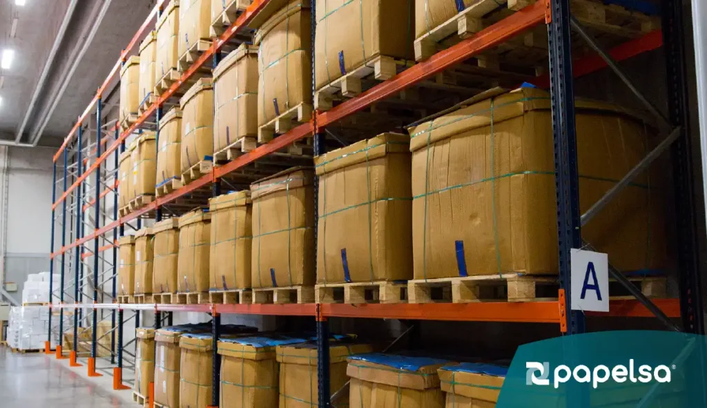 Almacén industrial con estanterías metálicas que almacenan empaques de cartón sobre pallets, cumpliendo con normas internacionales de empaque y transporte.