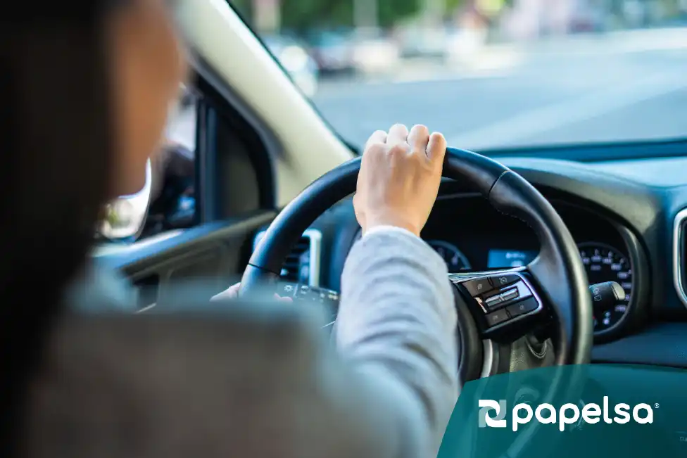 Persona conduciendo un automóvil, vista desde el asiento del copiloto enfocando sus manos en el volante.