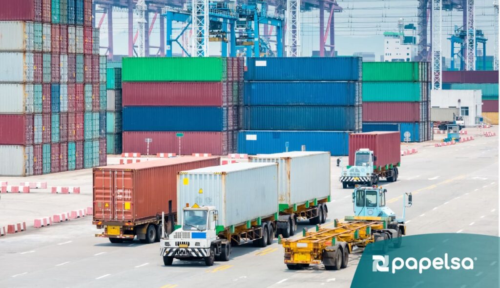 Transporte de contenedores en puerto industrial con camiones y grúas, mostrando logística, manejo de carga y distribución de mercancías.