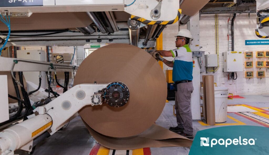 Operario supervisando maquinaria industrial para producción de papel en planta manufacturera.